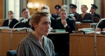 Movie still from “The Reader” (2008), directed by Stephen Daldry – A woman standing in front of a group of people; Medium shot, Over the shoulder angle