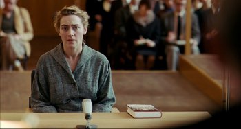 Movie still from “The Reader” (2008), directed by Stephen Daldry – A person sitting at a table with a book in front of them; Medium shot, Over the shoulder angle