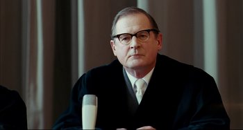 Movie still from “The Reader” (2008), directed by Stephen Daldry – A man in a black robe and white tie sitting in front of a microphone; Close Up shot, Low angle