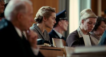 Movie still from “The Reader” (2008), directed by Stephen Daldry – A woman sitting in front of a group of people; Close Up shot, Over the shoulder angle