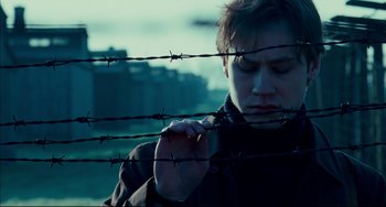 Movie still from “The Reader” (2008), directed by Stephen Daldry – A man standing next to a barbed wire fence; Close Up shot, Low angle