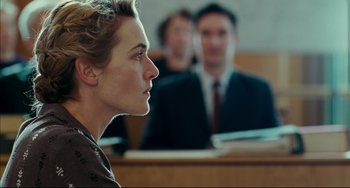 Movie still from “The Reader” (2008), directed by Stephen Daldry – A woman sitting in front of two other men in a courtroom; Close Up shot, Over the shoulder angle