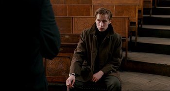 Movie still from “The Reader” (2008), directed by Stephen Daldry – A young man sitting on a bench in a room; Medium shot, Over the shoulder angle