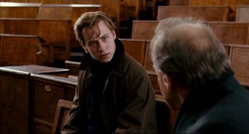 Movie still from “The Reader” (2008), directed by Stephen Daldry – A young man sitting next to an older man in a courtroom; Medium shot, Over the shoulder angle