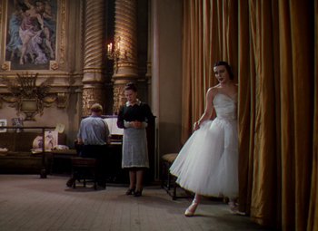 Movie still from “The Red Shoes” (1948), directed by Michael Powell – A woman in a white dress standing in front of a piano; Wide shot, Low angle