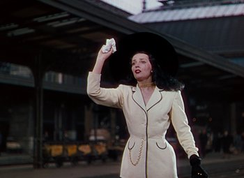 Movie still from “The Red Shoes” (1948), directed by Michael Powell – A woman in a white dress and a black hat holding up a white umbrella; Medium shot, Low angle