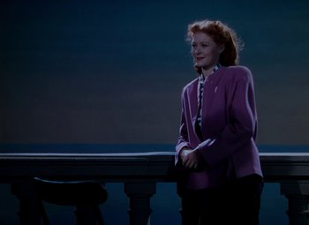 Movie still from “The Red Shoes” (1948), directed by Michael Powell – A woman in a purple jacket standing next to a table; Medium shot, High angle