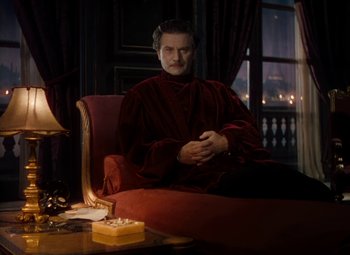 Movie still from “The Red Shoes” (1948), directed by Michael Powell – A man sitting on a red chair in a room; Medium shot, Over the shoulder angle