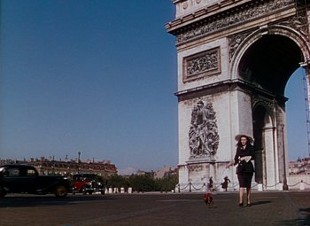 Movie still from “The Red Shoes” (1948), directed by Michael Powell – A woman walking a dog in front of a building; Extreme Wide shot, Low angle