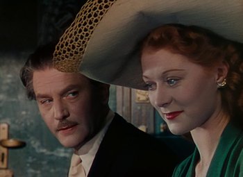 Movie still from “The Red Shoes” (1948), directed by Michael Powell – A man and a woman wearing a hat and posing for a picture; Close Up shot, Low angle