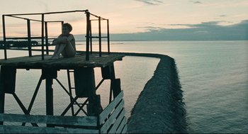 Movie still from “The Return” (2003), directed by Andrey Zvyagintsev – A man sitting on a platform next to the ocean; Extreme Wide shot, Low angle