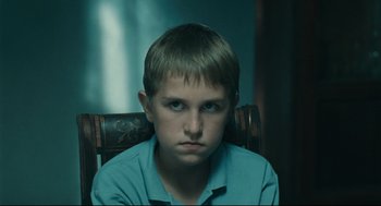 Movie still from “The Return” (2003), directed by Andrey Zvyagintsev – A young boy sitting in a chair looking at the camera; Close Up shot, Over the shoulder angle