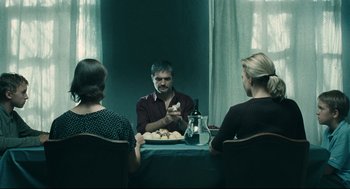 Movie still from “The Return” (2003), directed by Andrey Zvyagintsev – Three people sitting at a table with a plate of food on it; Medium shot, Over the shoulder angle