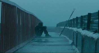 Movie still from “The Return” (2003), directed by Andrey Zvyagintsev – A man sitting on the side of a road in the rain; Wide shot, Low angle