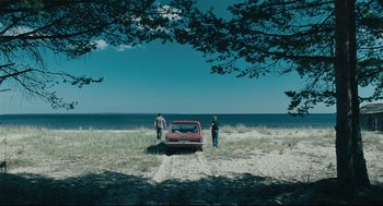 Movie still from “The Return” (2003), directed by Andrey Zvyagintsev – Two people standing next to a car on the beach; Extreme Wide shot, High angle