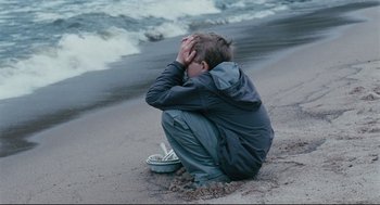 Movie still from “The Return” (2003), directed by Andrey Zvyagintsev – A boy sitting on the beach with his head in his hands; Medium shot, High angle