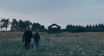 Movie still from “The Return” (2003), directed by Andrey Zvyagintsev – Two people walking in a field near a building; Extreme Wide shot, Low angle
