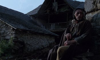 Movie still from “The Return of Martin Guerre” (1982), directed by Daniel Vigne – A man sitting on the ground in front of an old house; Medium shot, Low angle