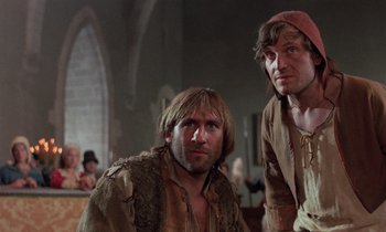 Movie still from “The Return of Martin Guerre” (1982), directed by Daniel Vigne – Two men in medieval garb sitting in front of a crowd; Medium shot, Low angle