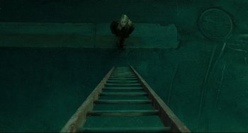 Movie still from “The Ring” (2002), directed by Gore Verbinski – A person standing on a ladder in a room; Wide shot, Overhead angle