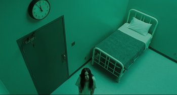 Movie still from “The Ring” (2002), directed by Gore Verbinski – A woman standing next to a bed in a green room; Wide shot, High angle