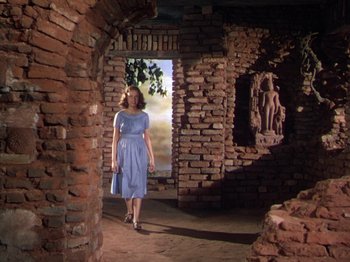 Movie still from “The River” (1951), directed by Jean Renoir – A woman in a blue dress standing in an old brick building; Wide shot, Low angle
