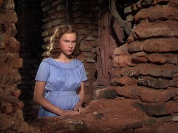 Movie still from “The River” (1951), directed by Jean Renoir – A woman in a blue dress standing next to a pile of rubble; Medium shot, Low angle