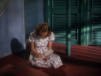 Movie still from “The River” (1951), directed by Jean Renoir – A young girl sitting on the ground writing on a piece of paper; Medium shot, High angle