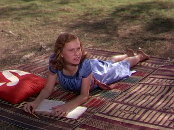 Movie still from “The River” (1951), directed by Jean Renoir – A young girl laying on the ground reading a book; Medium shot, High angle