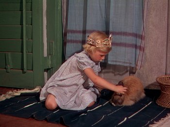 Movie still from “The River” (1951), directed by Jean Renoir – A little girl wearing a crown petting a cat on the floor; Medium shot, High angle
