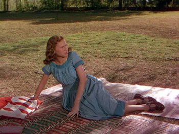 Movie still from “The River” (1951), directed by Jean Renoir – A young woman in a blue dress is laying on the ground; Wide shot, High angle
