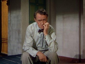 Movie still from “The River” (1951), directed by Jean Renoir – A man sitting on the ground with his hand on his face; Medium shot, High angle