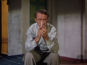 Movie still from “The River” (1951), directed by Jean Renoir – A man sitting on the ground holding a glass; Medium shot, High angle