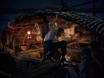 Movie still from “The River” (1951), directed by Jean Renoir – A man standing on the side of a boat at night; Wide shot, High angle