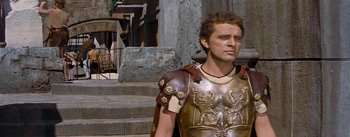 Movie still from “The Robe” (1953), directed by Henry Koster – A man in a roman soldier's outfit stands in front of a stone building; Medium shot, Low angle