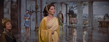 Movie still from “The Robe” (1953), directed by Henry Koster – A woman in a yellow dress standing in front of statues; Medium shot, Over the shoulder angle