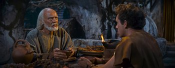 Movie still from “The Robe” (1953), directed by Henry Koster – A man sitting at a table in front of two other men; Medium shot, Over the shoulder angle