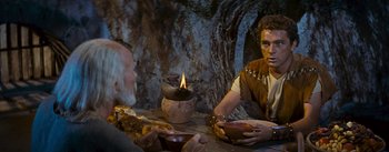 Movie still from “The Robe” (1953), directed by Henry Koster – Two men are sitting at a table with food; Medium shot, Over the shoulder angle