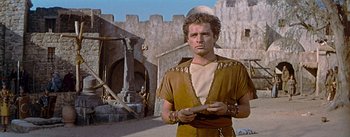 Movie still from “The Robe” (1953), directed by Henry Koster – A man in a brown and tan outfit holding a wooden stick; Medium shot, Low angle