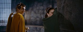 Movie still from “The Robe” (1953), directed by Henry Koster – A man and a woman standing next to each other in front of a brick wall; Medium shot, Low angle