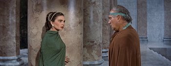 Movie still from “The Robe” (1953), directed by Henry Koster – A man and a woman standing next to each other in front of pillars; Medium shot, Over the shoulder angle