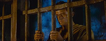 Movie still from “The Robe” (1953), directed by Henry Koster – A man holding onto a metal bar in a jail cell; Close Up shot, Low angle