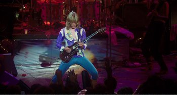 Movie still from “The Rose” (1979), directed by Mark Rydell – A man playing a guitar on a stage with people watching; Wide shot, High angle