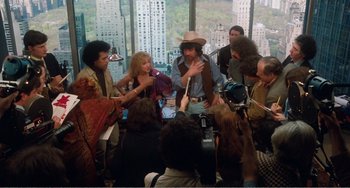 Movie still from “The Rose” (1979), directed by Mark Rydell – A group of people standing around a table; Wide shot, High angle