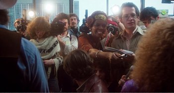Movie still from “The Rose” (1979), directed by Mark Rydell – A crowd of people gathered around a woman; Medium shot, Over the shoulder angle