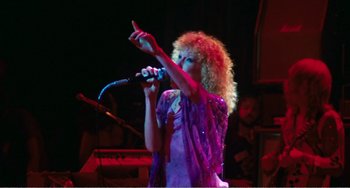 Movie still from “The Rose” (1979), directed by Mark Rydell – A woman with curly hair is singing into a microphone; Medium shot, Low angle