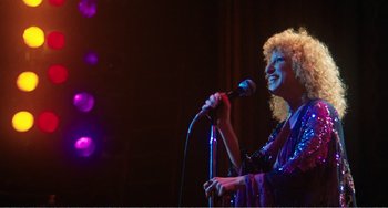 A woman with curly blonde hair singing into a microphone