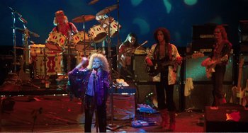 Movie still from “The Rose” (1979), directed by Mark Rydell – A group of people on a stage with a microphone; Wide shot, Low angle