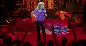 Movie still from “The Rose” (1979), directed by Mark Rydell – A woman in a purple shirt is on a stage singing; Wide shot, High angle