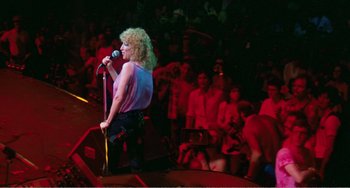 Movie still from “The Rose” (1979), directed by Mark Rydell – A woman with curly blonde hair singing into a microphone; Wide shot, Low angle